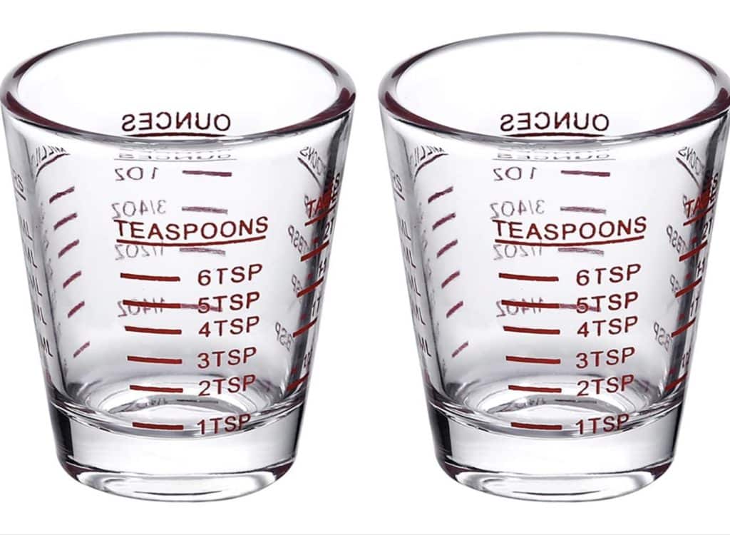 Two clear glass measuring cups with red markings are perfect for crafting a strawberry basil cocktail. Each displays gradients from 1 to 6 teaspoons and from 0.5 to 2 ounces, ideal for precise mixing. The cups rest side by side on a white background, ready for your next creation.